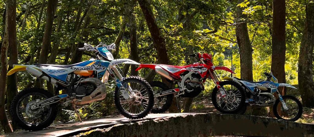 Three enduro bikes parked on a bridge in the woods.