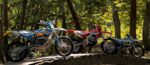 Three enduro bikes parked on a bridge in the woods.